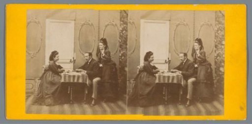 Man and a woman sitting at a table in a setting, a second woman leaning against the man's chair