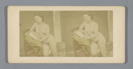 Nude woman seated on a sofa with a book