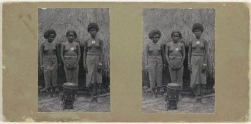 Three women standing before a thatched roof near a drum