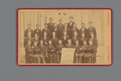 Group portrait with about twenty young men and several Catholic priests, in the foreground a board with the inscription: 'Late sejunctI concordia usque jungemur'