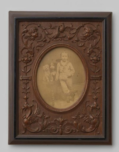 Portrait of an unknown boy leaning on a chair with two dogs on it