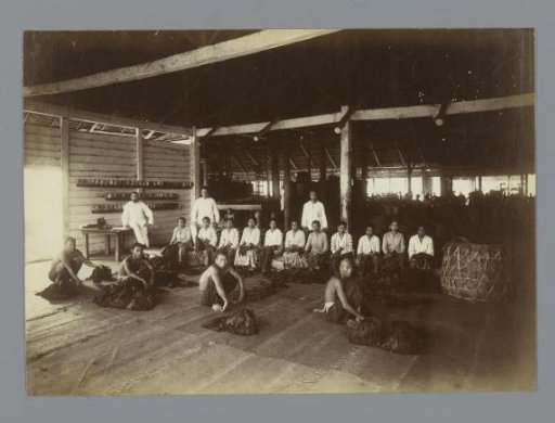 Group portrait of local contract workers and two European men in a tobacco drying shed