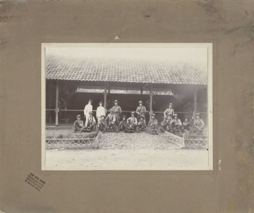 Group portrait of KNIL soldiers with machine guns in front of a stable