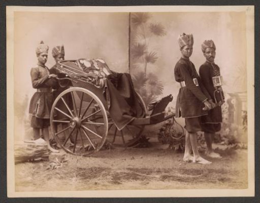 Studio portrait of four Indian men in uniform with a carriage, India