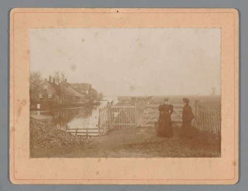 Two women in front of a fence, with a farm in the background
