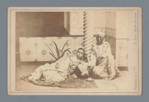 Two people in traditional dress by a pillar in Algeria