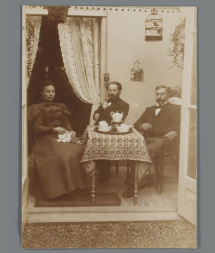 Portrait of two unknown men, one with a pipe, and an unknown woman with crochet work around a table with tea service