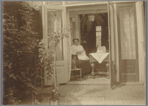 Woman with needlework in a living room, seen from the garden