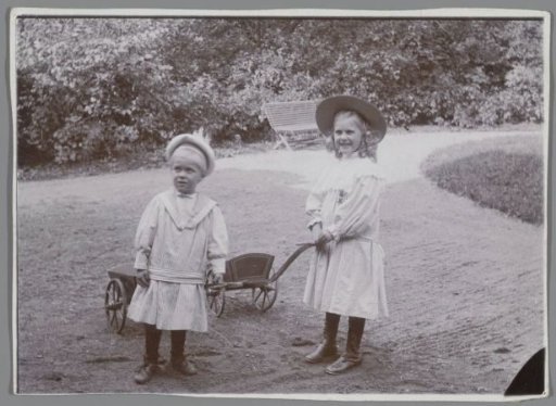 Portrait of two unknown children with carriages in a garden