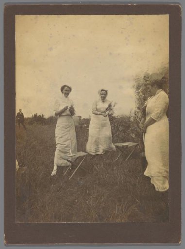 Three Women Lighting a Candle Outdoors, with a Man Standing in the Distance