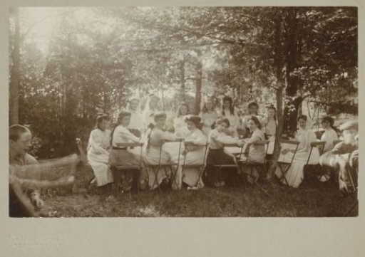 Group portrait of unknown young women seated at a table in a forest or park