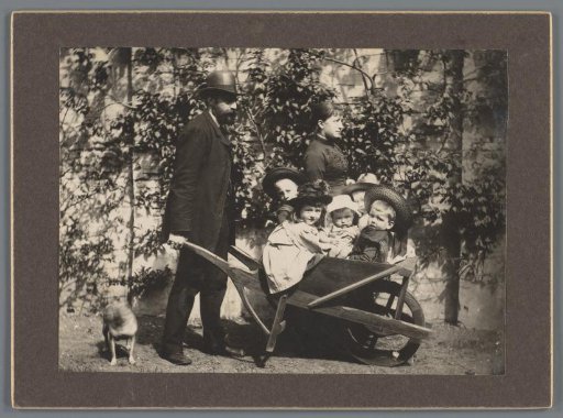 Man and Woman Walking with a Dog and a Wheelbarrow Containing Five Children