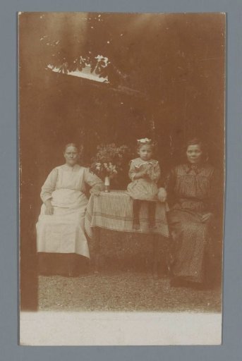 Portrait of two unknown women and a girl at a table in a garden