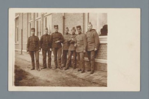 Group portrait of seven soldiers in uniform in front of a building