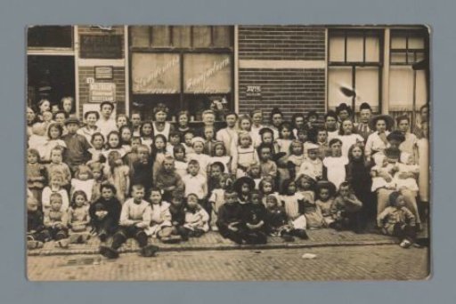 Group portrait of children and unknown women in front of a grocery store (presumably) in Westzaan