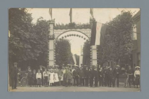 Group portrait of unknown people in a street with a triumphal arch celebrating the independence of the Netherlands