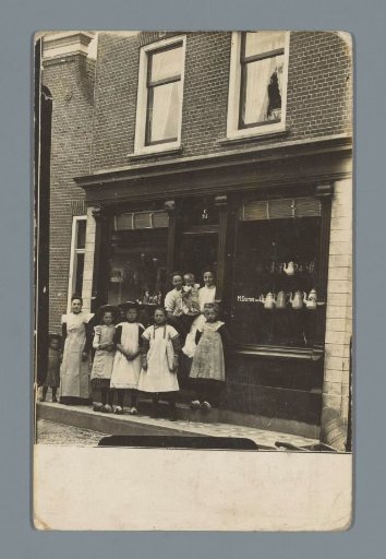 Group portrait of unknown women and children in front of the shop of M. Docters van Leeuwen