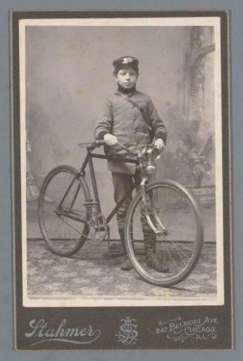 Studio portrait of an unknown boy in a uniform with a bicycle