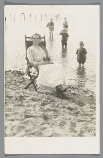 Portrait of an unknown woman in a folding chair on the beach, with four children in the background