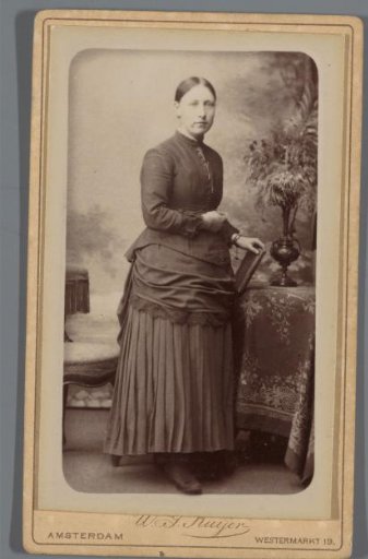Portrait of an unknown woman, standing beside a table with a book in her hands