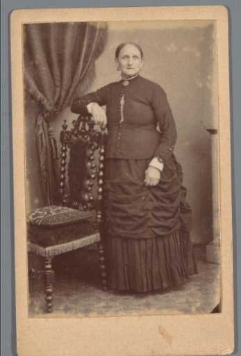 Portrait of an unknown woman, standing beside a chair