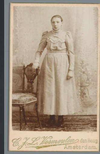 Portrait of an unknown woman, standing beside a chair