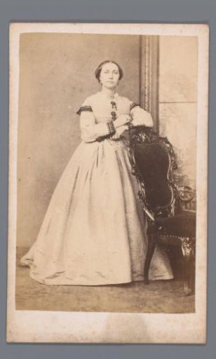 Portrait of an unknown woman, standing beside a chair