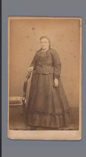 Portrait of an unknown woman, standing beside a chair