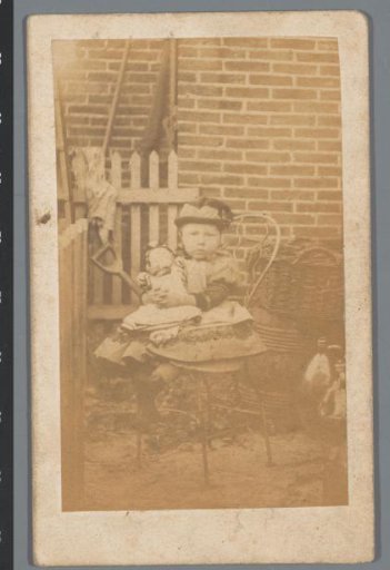 Portrait of an unknown child with a doll on a chair outside