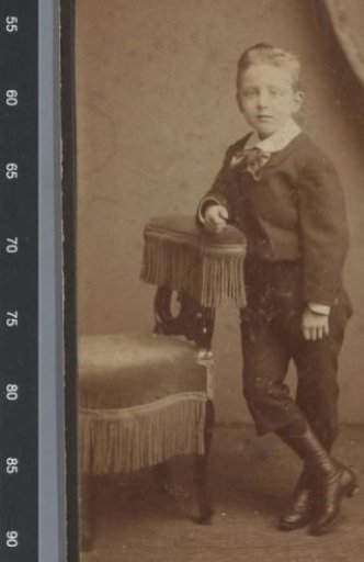 Portrait of an unknown boy beside a chair