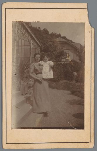 Portrait of an unknown woman with a baby outside in front of a house