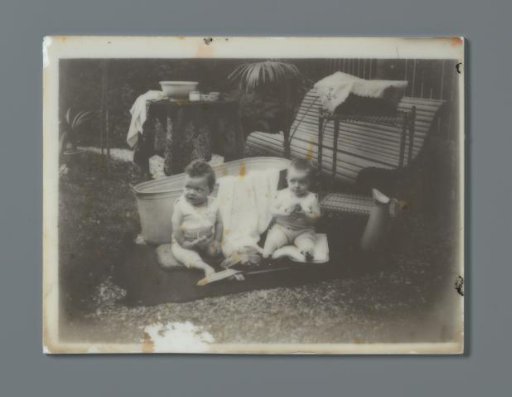Two toddlers sitting on a cloth near a bench and a bathtub, probably the twins Ad and Johanna van der Kop