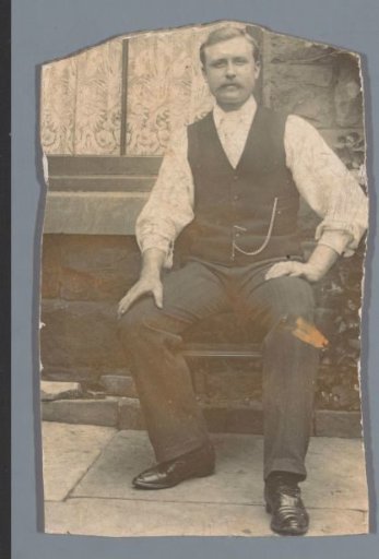 Portrait of an unknown man sitting on a chair before a house