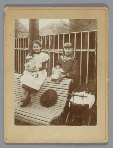 Portrait of two unknown girls with dolls next to a pram