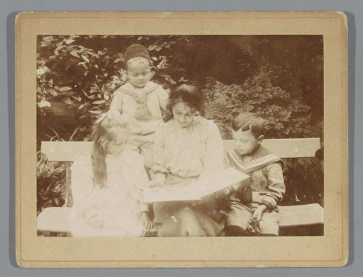 Young woman reading a book to three children on a bench