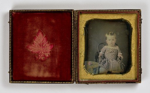 Untitled (Girl in Checkered Dress, Seated by a Table with a Flower)